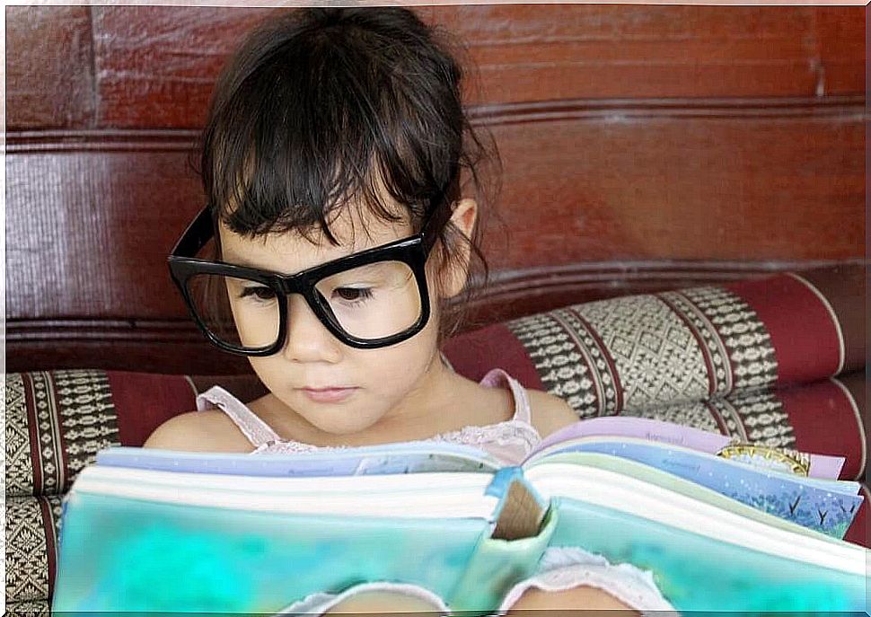 Little girl with glasses reads in bed