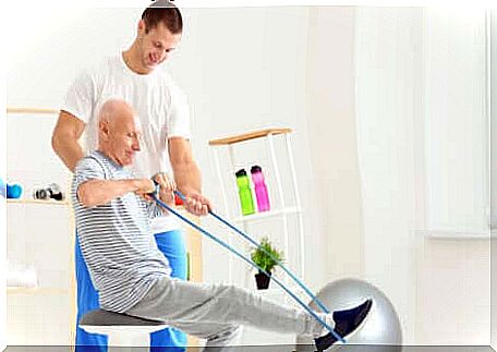 Elderly man performs rowing with elastic band.