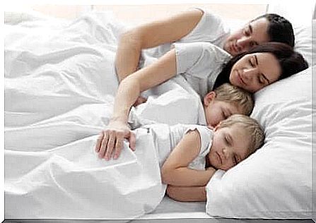 Twins sleep in the bed with mom and dad.